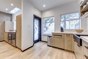 A modern kitchen with wooden cabinets, a built-in dishwasher, and a large window with blinds.