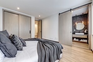 Un dormitorio moderno con una cama grande, una puerta corredera que da a un baño y una zona de lavamanos visible.