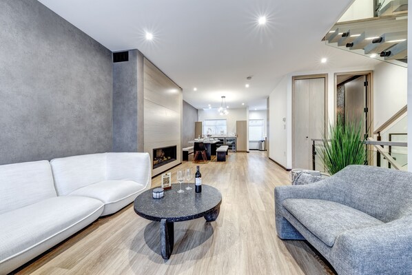 A modern living room with a white sofa, a grey armchair, and a round coffee table with wine glasses and a bottle.