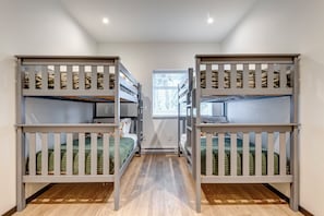 Een kamer met stapelbedden, een raam met zonwering en een houten vloer.