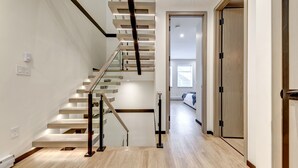 Een modern interieur met een houten trap, een gang die naar een slaapkamer leidt, en een houten deur.