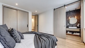 Een moderne slaapkamer met een groot bed, een kledingkast en een badkamer met een wastafel en spiegel.