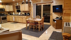 A wooden interior with a dining table and chairs, a kitchen with wooden cabinets, a ceiling fan, and a television. - River Front Cabin with Mountain Views (Jay)