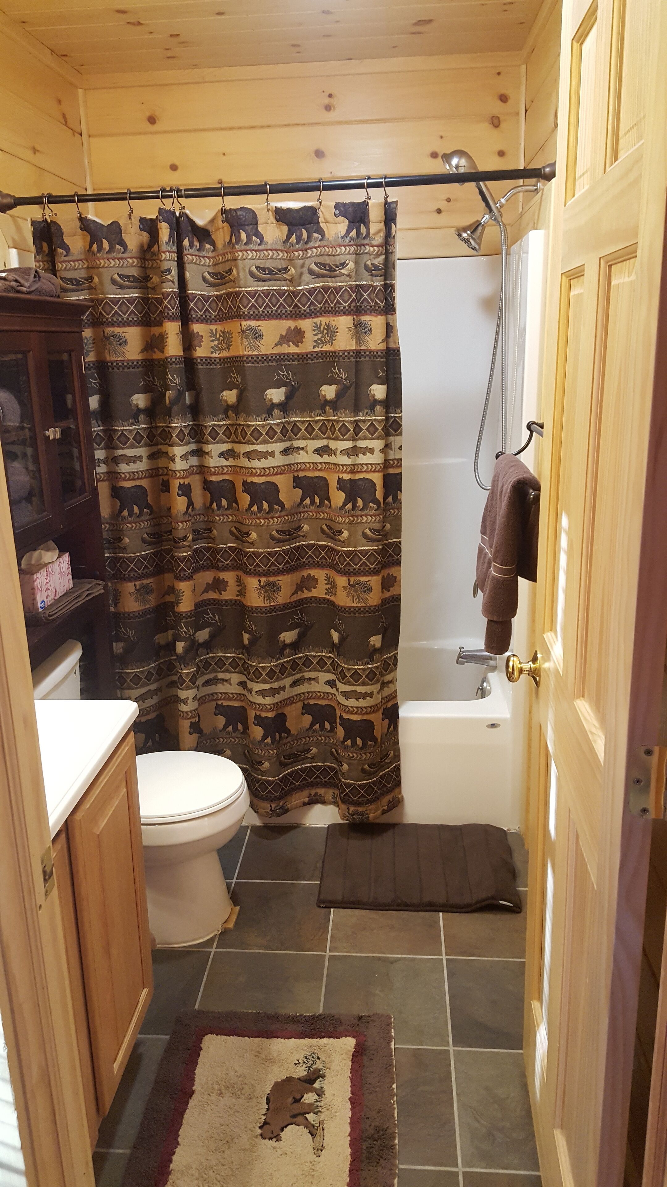 Een kleine, praktische badkamer met een douchegordijn met dierenprint, een toilet, een bad en een houten deur.