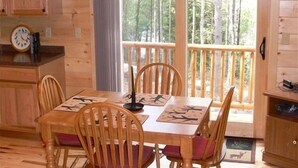 A wooden cabin interior with a dining table, chairs, a ceiling fan, and a view of the forest through large windows. - River Front Cabin with Mountain Views (Jay)