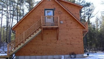 Surrounded by trees, this cabin features a steep staircase leading to a balcony.