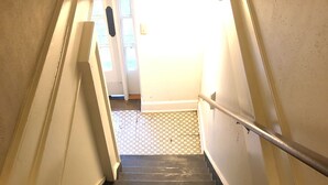Eine Holztreppe mit Metallhandlauf, die zu einem Raum mit gefliestem Boden und einer Tür führt.