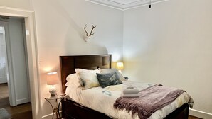 Ein ordentlich bezogenes Bett mit Holz-Kopfschild, zwei Nachttischlampen und einem dekorativen Geweih an der Wand.