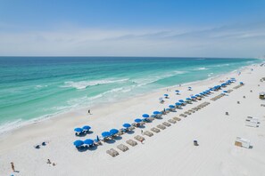 Une plage bordée de rangées de parasols et de chaises de plage, un rivage sablonneux et l’océan.