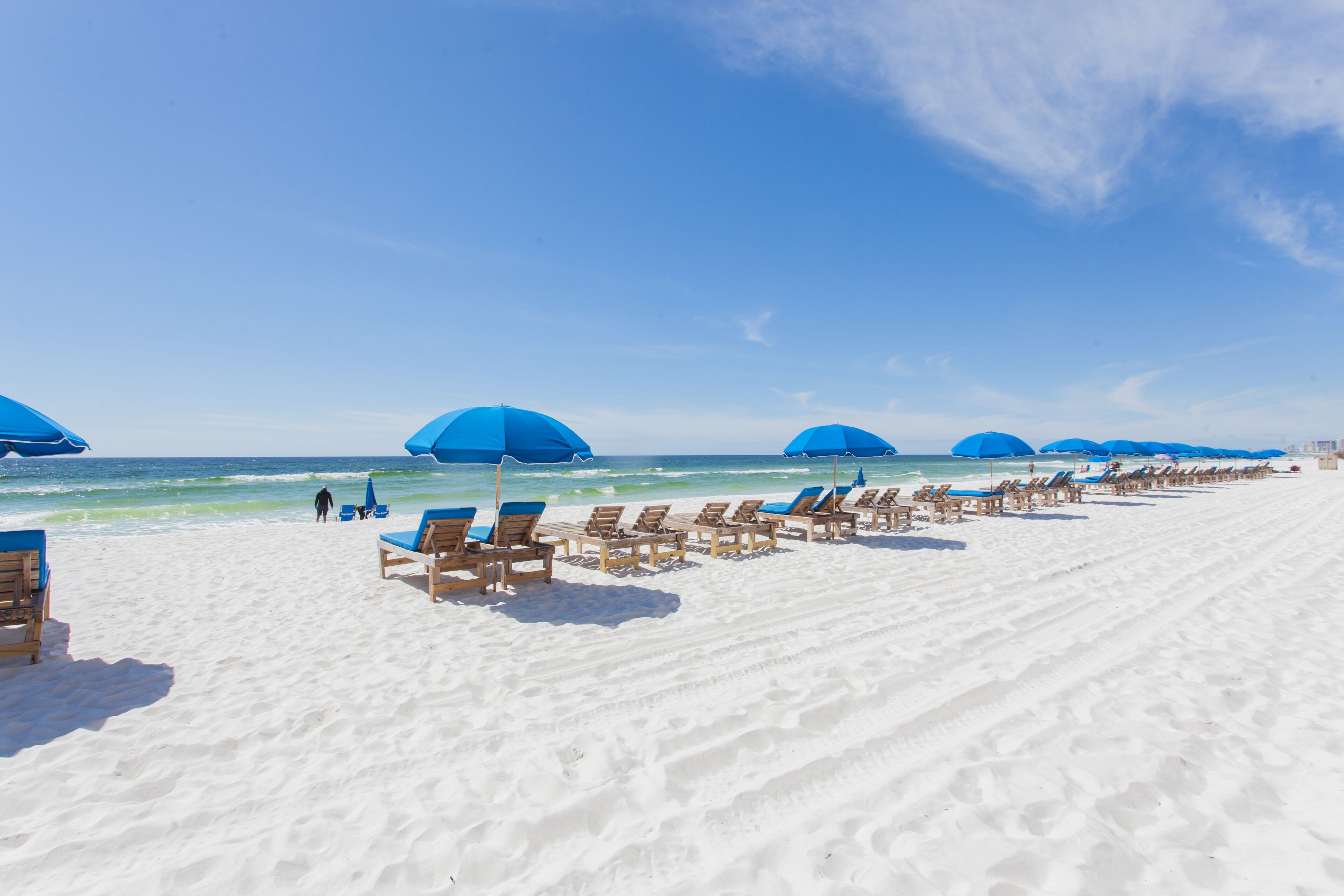 A beach with rows of sun loungers and umbrellas, a clear sky, and the ocean in the background.