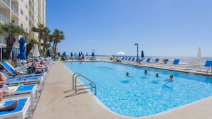 Une piscine entourée d’un bâtiment d’hôtel, avec des chaises longues et des parasols.