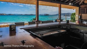 A restaurant with a view of the ocean, featuring wooden beams, a bar area, and outdoor seating. - Gorgeous boho at the beach walkout oceanfront condo in Sapphire D building. (St Thomas)