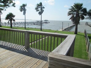 A wooden deck with a railing overlooking a marina with boats and palm trees.