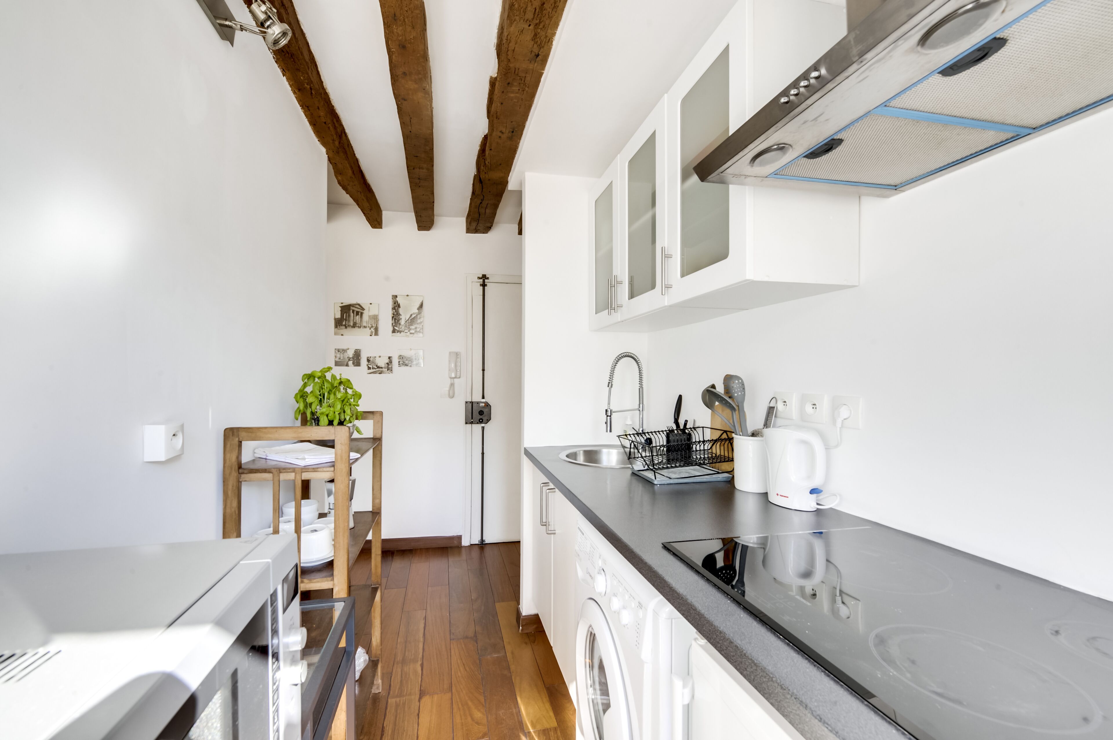 A compact kitchen with wooden beams, white cabinets, a washing machine, and a sink.