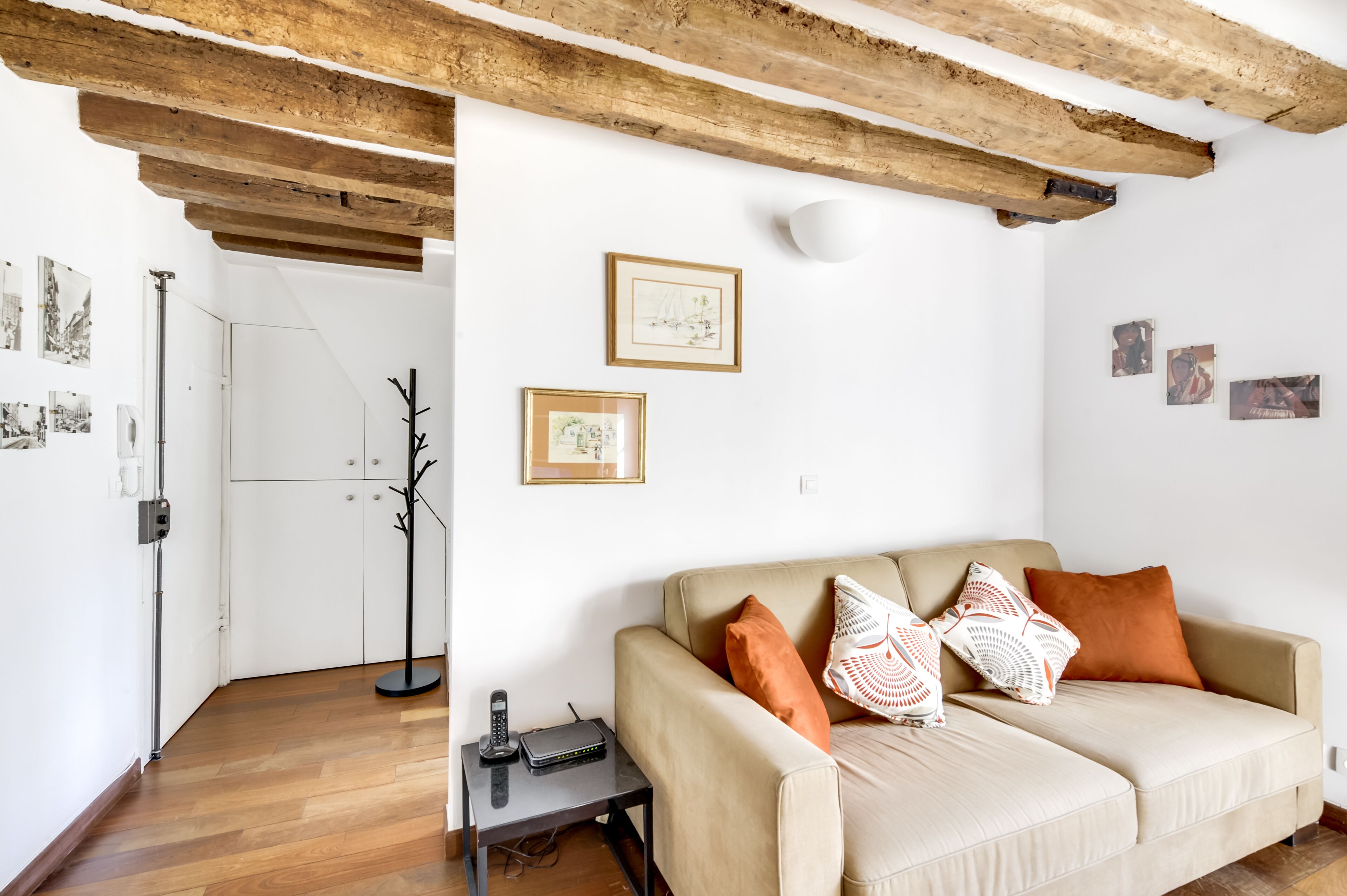 Ein Wohnzimmer mit einer Couch, einem Kleiderständer und gerahmten Bildern an der Wand.