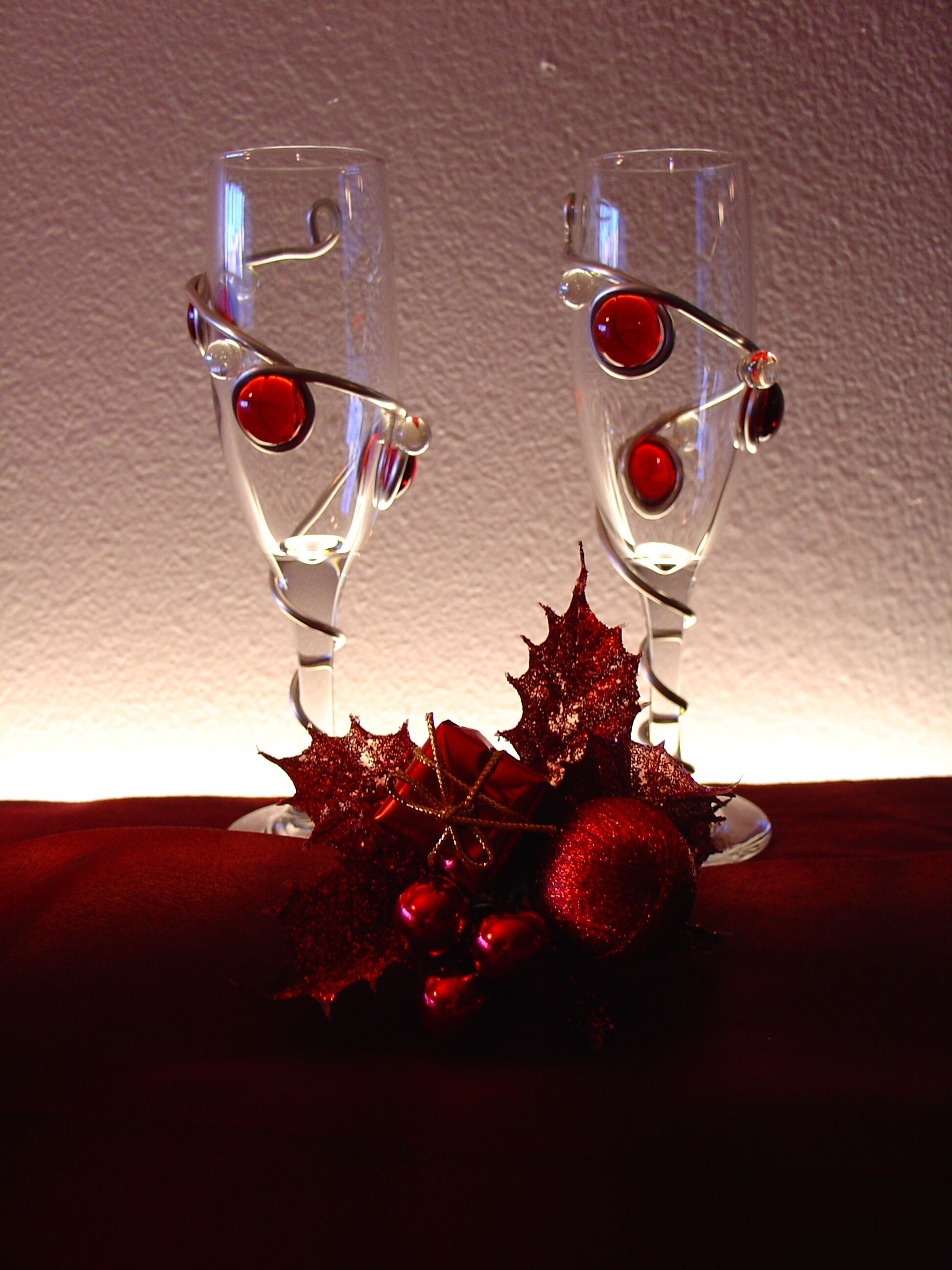 Two glasses with red liquid, decorated with red ornaments and a bow, on a dark surface.