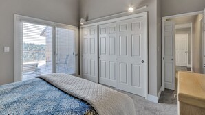 Ein Schlafzimmer mit einem Bett, einem Schrank mit weißen Türen und einer Glasschiebetür, die auf einen Balkon führt.