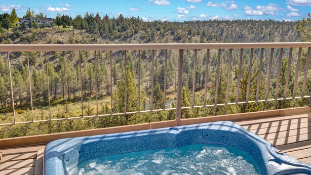 Ein Whirlpool auf einer Holzterrasse mit Blick auf einen bewaldeten Hügel.
