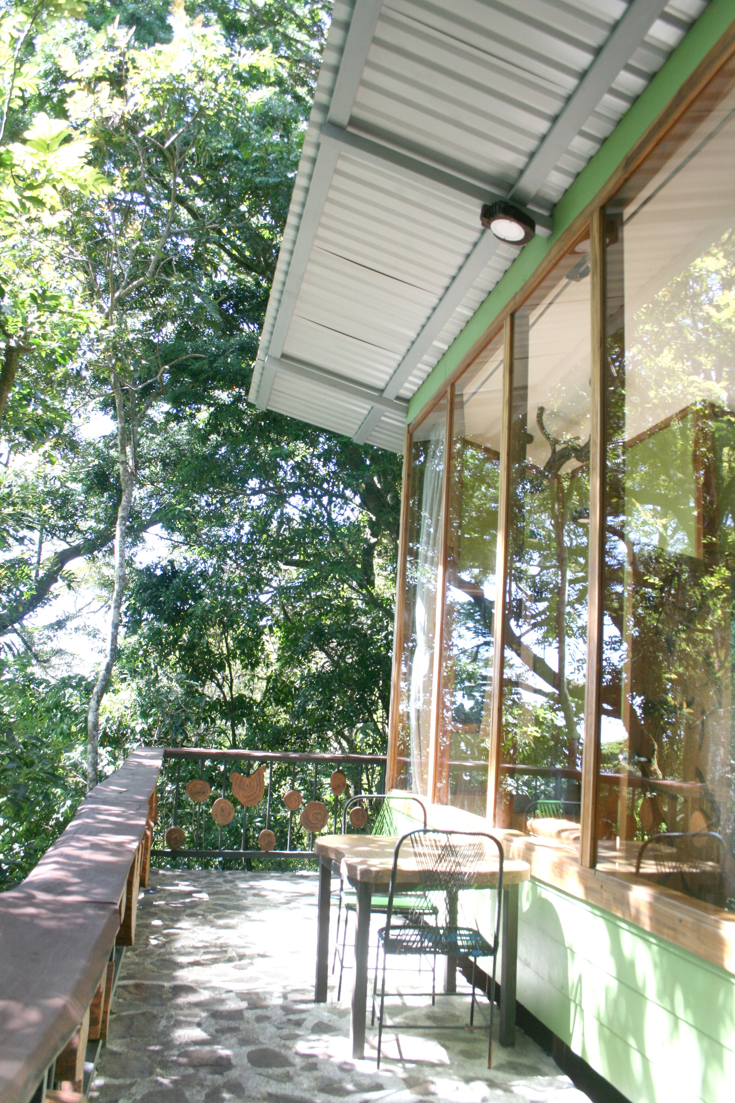 A covered outdoor seating area with stone flooring, wooden benches, and a table with chairs.