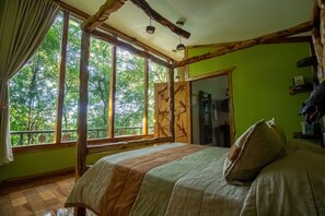 Une pièce dotée d’une grande fenêtre, de poutres apparentes, d’un lit recouvert d’une couvre-lit à rayures et d’un mur vert.