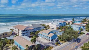 A coastal town with beachfront properties, including multi-story buildings with balconies and a road leading to the beach.