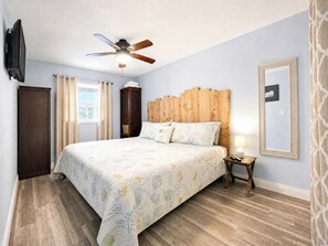 A bedroom with a bed, wooden headboard, ceiling fan, bedside lamp, and a TV mounted on the wall. - 2 Bedroom In Indian Rocks Beach, FL - Gulf Side Complex w/ Direct Beach Access (Indian Rocks Beach)