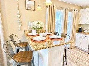 A dining area with a granite countertop, white plates, and a vase of flowers. - 2 Bedroom In Indian Rocks Beach, FL - Gulf Side Complex w/ Direct Beach Access (Indian Rocks Beach)