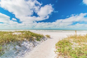 A sandy beach path leading to the ocean with sparse vegetation.