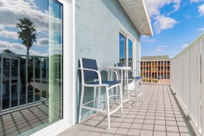 A balcony with white chairs and a table, a building with large windows, and a clear sky.