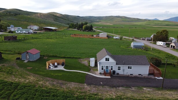 Paisagem rural com uma casa branca, um pequeno galpão azul e um deck de madeira.