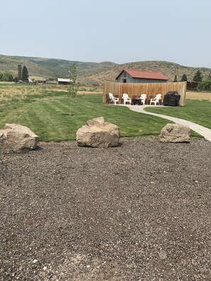 A gravel patio with large rocks, a wooden fence, and a covered outdoor seating area with chairs and a barbecue grill.