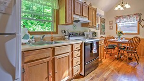 A kitchen with wooden cabinets, a stainless steel stove, and a dining area with wooden chairs. -  HOT TUB,WIFI, JACUZZI, FIRE PIT, ~A/C~ CREEK, 2 MIN TO MAGGIE (Maggie Valley)