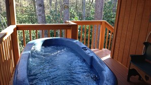 A hot tub on a wooden deck with a view of trees. -  HOT TUB,WIFI, JACUZZI, FIRE PIT, ~A/C~ CREEK, 2 MIN TO MAGGIE (Maggie Valley)