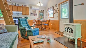 A cozy living room with a blue armchair, wooden dining table, and a vintage stove. -  HOT TUB,WIFI, JACUZZI, FIRE PIT, ~A/C~ CREEK, 2 MIN TO MAGGIE (Maggie Valley)