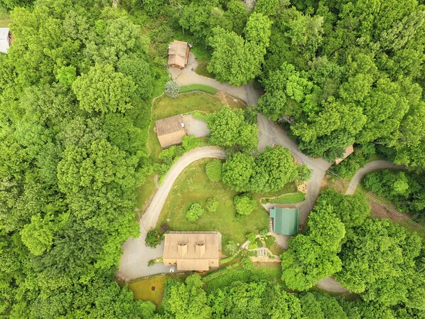 An aerial view of a property with a large building, several smaller structures, and surrounding dense greenery.