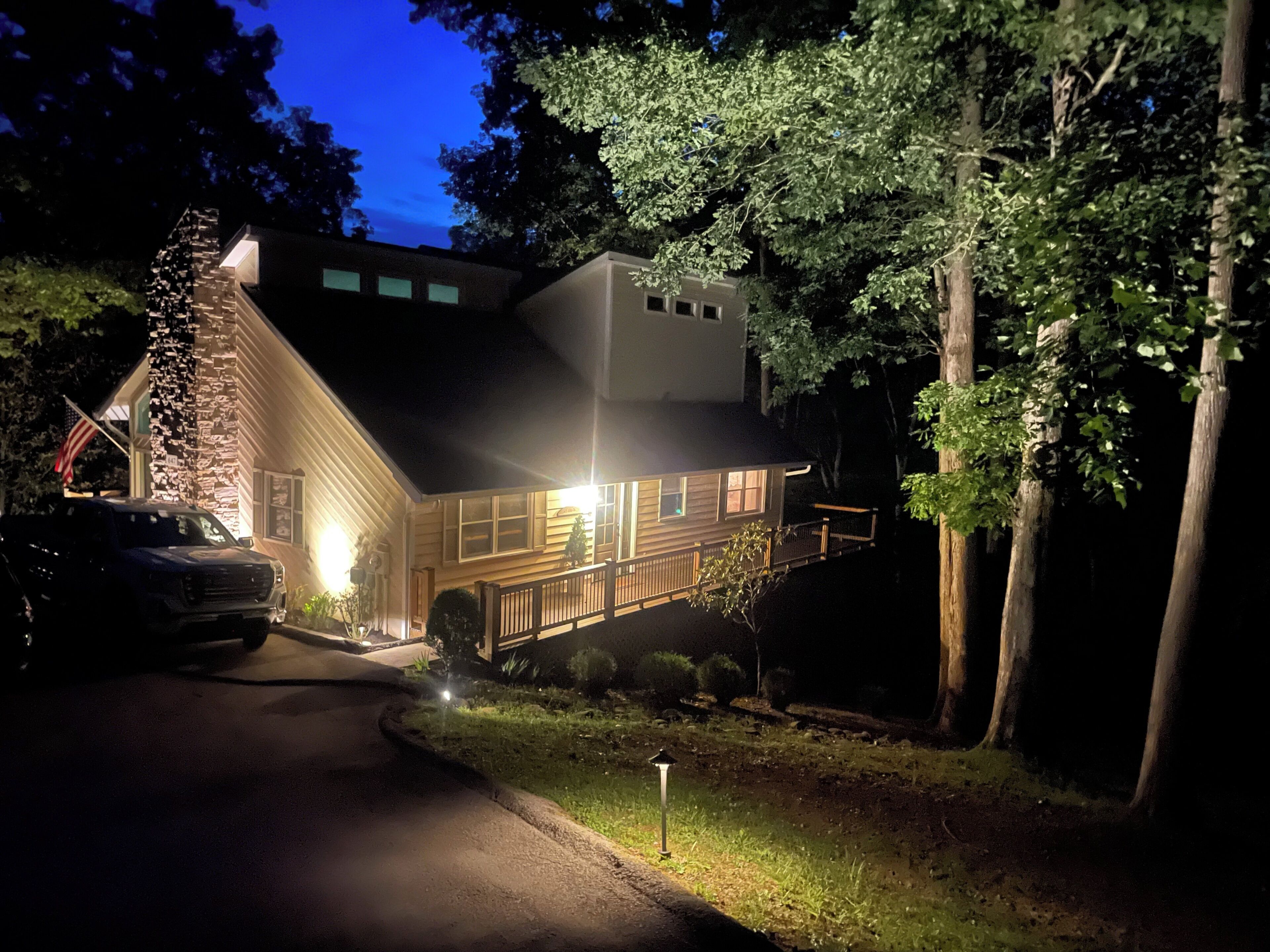 A two-story house with a visible garage, a well-lit front porch, and a small deck.