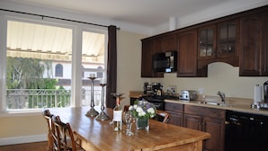 Une cuisine avec des meubles en bois, une table à manger avec des chaises, une fenêtre avec des rideaux et une vue sur la verdure à l’extérieur.