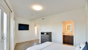 A bedroom with a bed, a dresser, a TV, and a bathroom with a mirror and sink. - Walk to the Waterfront: Spacious Condo in the Heart of Newport (Newport)