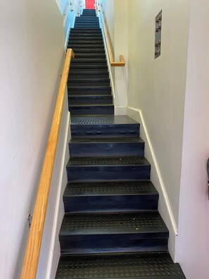 A staircase with a wooden handrail and a metal banister, leading to a red door at the top.