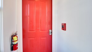 A red door with a fire alarm and a fire extinguisher mounted on the wall. - Walk to the Waterfront: Spacious Condo in the Heart of Newport (Newport)