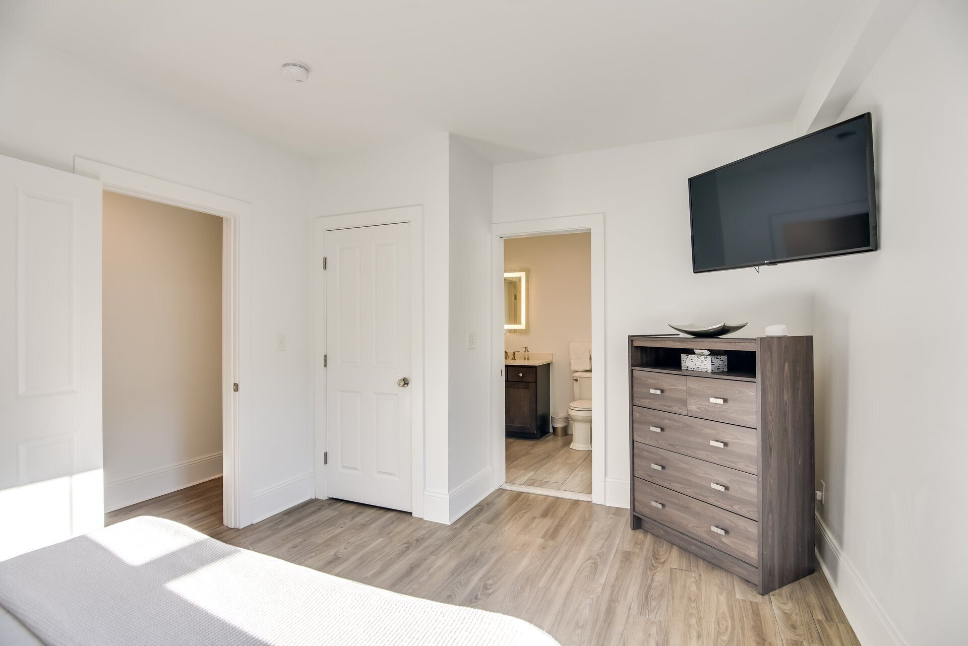 A bedroom with a bed, a dresser, a TV, and a bathroom visible through an open door.
