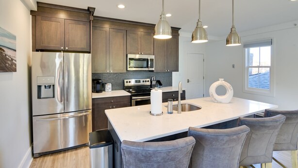 A modern kitchen with stainless steel appliances, a central island with bar stools, and pendant lighting. - Walk to the Waterfront: Spacious Condo in the Heart of Newport (Newport)