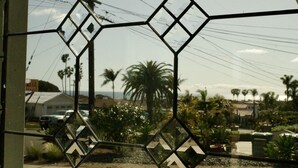 A view through a window with a geometric pattern, palm trees, and a road in the background. - 3 Bed 2 Bath Ocean View Home (Carlsbad)