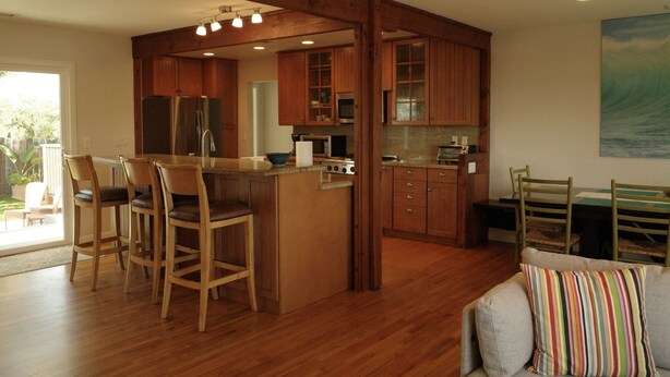 A kitchen with wooden cabinets, a central island with bar stools, a dining table with chairs, and a painting on the wall. - 3 Bed 2 Bath Ocean View Home (Carlsbad)