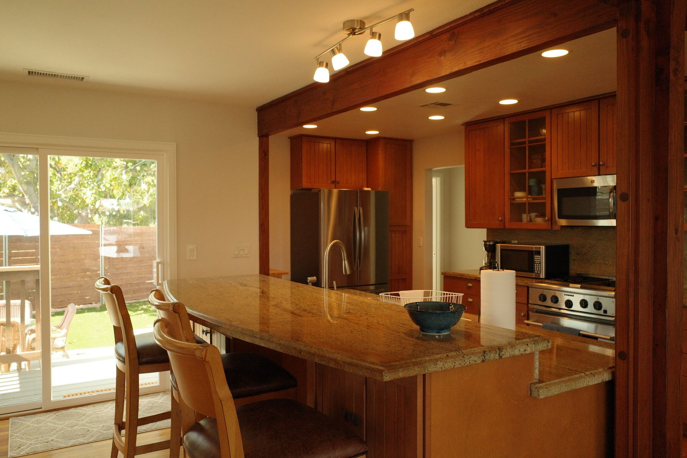 Una cocina con armarios de madera, electrodomésticos de acero inoxidable, una isla grande con un lavabo y una puerta corrediza de vidrio al patio.