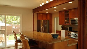 A kitchen with wooden cabinets, stainless steel appliances, a large island with a bowl, and a sliding glass door to the patio. - 3 Bed 2 Bath Ocean View Home (Carlsbad)