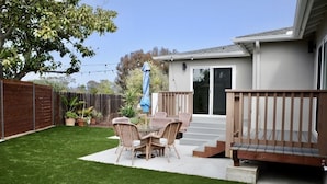 A backyard with a patio table and chairs, a wooden deck, and a house with a sliding glass door. - 3 Bed 2 Bath Ocean View Home (Carlsbad)