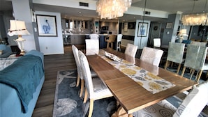 A modern dining area with a long wooden table, patterned chairs, and a chandelier. -  Luxury 2400 Sq Ft Condo w/ Epic Views, Private Beach Access, Large Pool (Siesta Key)