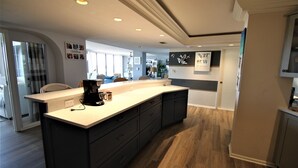 A modern kitchen with a large island, dark cabinetry, and a light countertop. -  Luxury 2400 Sq Ft Condo w/ Epic Views, Private Beach Access, Large Pool (Siesta Key)