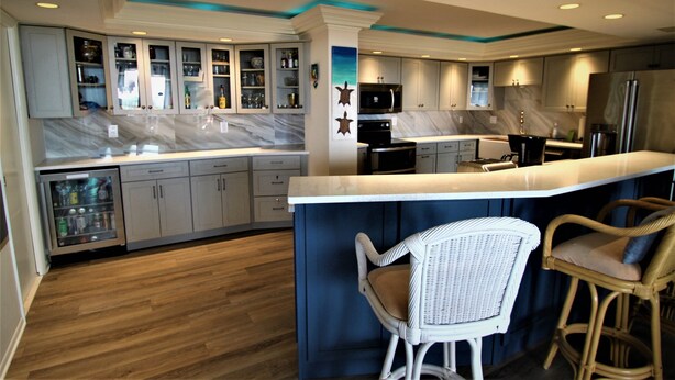 A modern kitchen with marble countertops, built-in cabinets, a central island with bar stools, and a refrigerator. -  Luxury 2400 Sq Ft Condo w/ Epic Views, Private Beach Access, Large Pool (Siesta Key)
